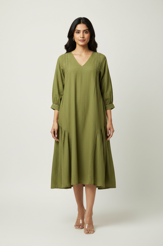 A woman modeling a loose olive green midi dress with three-quarter sleeves, a V-neckline, and subtle embroidered details, set against a plain light gray studio background.