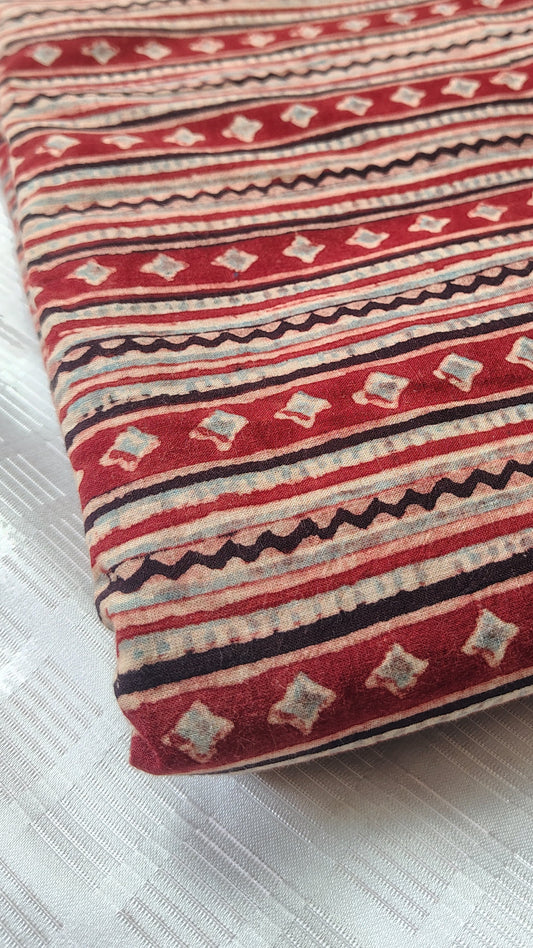 Decorative pillow with red and beige pattern on a white textured surface