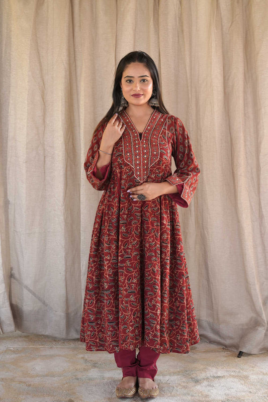 A woman wearing a red and blue block printed kurta with golden zari embroidery on the neck and sleeves, paired with matching red pants.