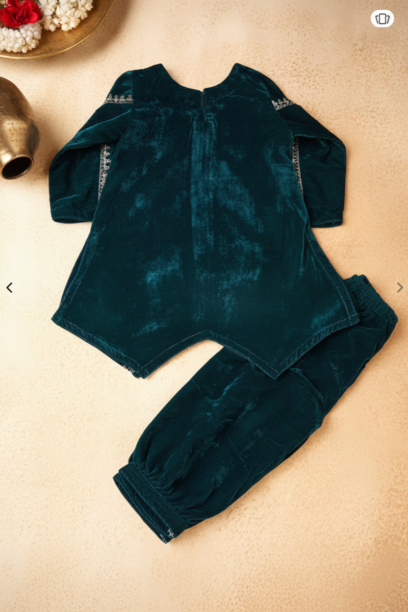 A dark blue velvet two-piece baby outfit set consisting of a long-sleeve romper and matching pants, laid flat on a textured beige background with decorative props.