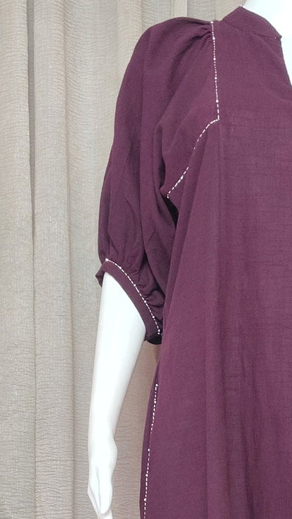 A dark purple short-sleeved dress displayed on a white mannequin, set against a draped beige fabric backdrop.