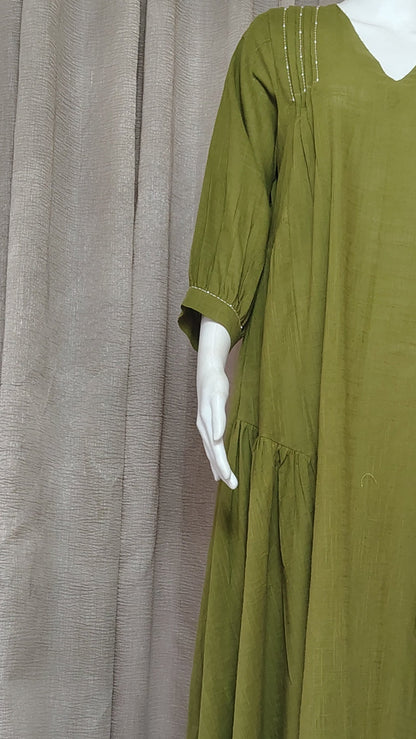 An olive green long-sleeve dress displayed on a white mannequin, set against a backdrop of draped gray fabric.