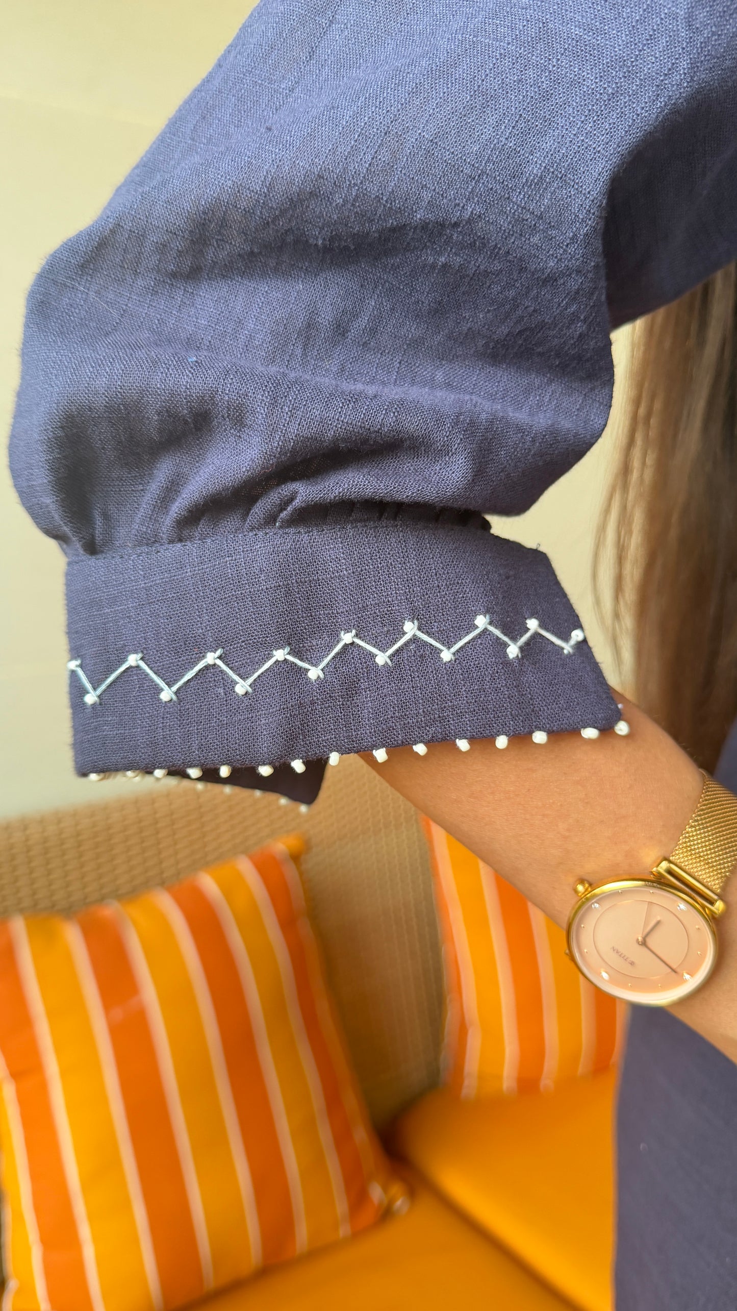 Person wearing a blue sleeve with white stitching detail, sitting on a yellow couch with orange cushions.