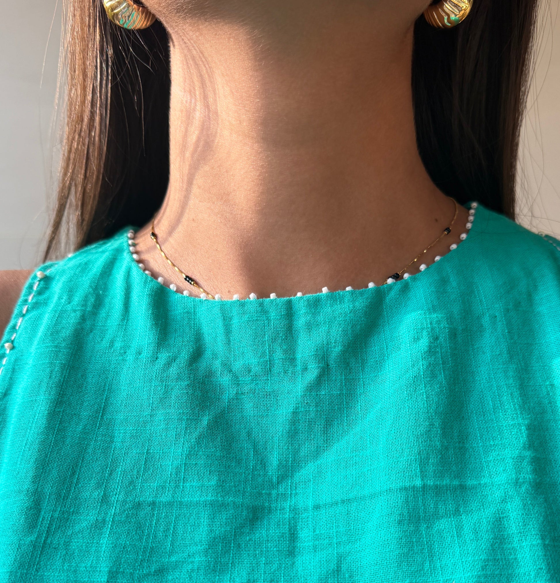 Person wearing a Cyan dress with a necklace and earrings.