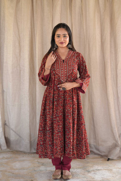 A woman wearing a red and blue block printed kurta with golden zari embroidery on the neck and sleeves, paired with matching red pants.